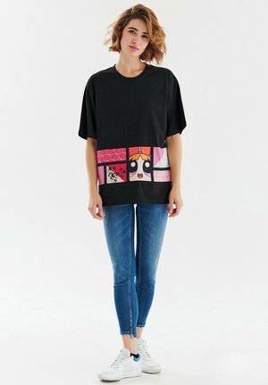 Czarna, oversize t-shirt z kolorowym nadrukiem graficznym na dole, przedstawiającym postacie z kreskówek. W połączeniu z niebieskimi, obcisłymi dżinsami i białymi trampkami.