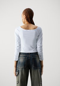 Hvit langermet topp med båt hals, kombinert med mørkeblå vide jeans i denim med lappe-lommer og en sidelomme.