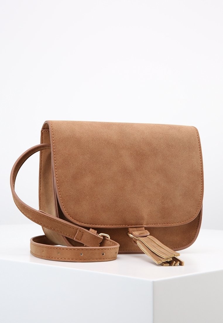 Bolso cruzado de imitación de ante marrón con cierre de solapa, correa ajustable y detalle de borlas. Textura suave sin patrones visibles.
