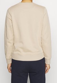 Sweat-shirt beige à manches longues, avec poignets et ourlet inférieur côtelés. Texture douce avec un col rond et un détail discret d'une couture au dos.