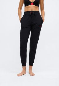 Black jogger pants with a drawstring waist, side pockets, and red logo accents. Smooth fabric with fitted cuffs at the ankles.