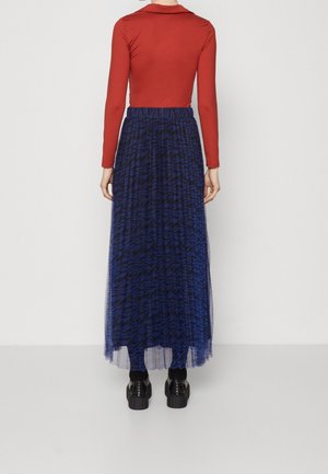 Haut rouge à manches longues associé à une jupe longue en tulle bleu ornée d'un motif abstrait subtil. Porté avec des chaussures à plateforme noires.