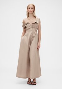 Beige, axelbandslös klänning med knäppning fram, kort krage, sidofickor och en lång, flödande silhuett. Slät bomullstyg.