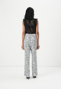 Top in pizzo nero con bordi a scalloped abbinato a pantaloni bianchi con un motivo astratto nero. Entrambi gli articoli hanno una silhouette aderente.