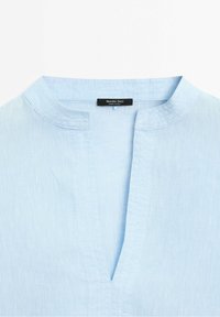 Encolure d'une chemise en lin bleu clair avec un petit col et une fente en V profonde, comportant une étiquette Massimo Dutti à l'intérieur.