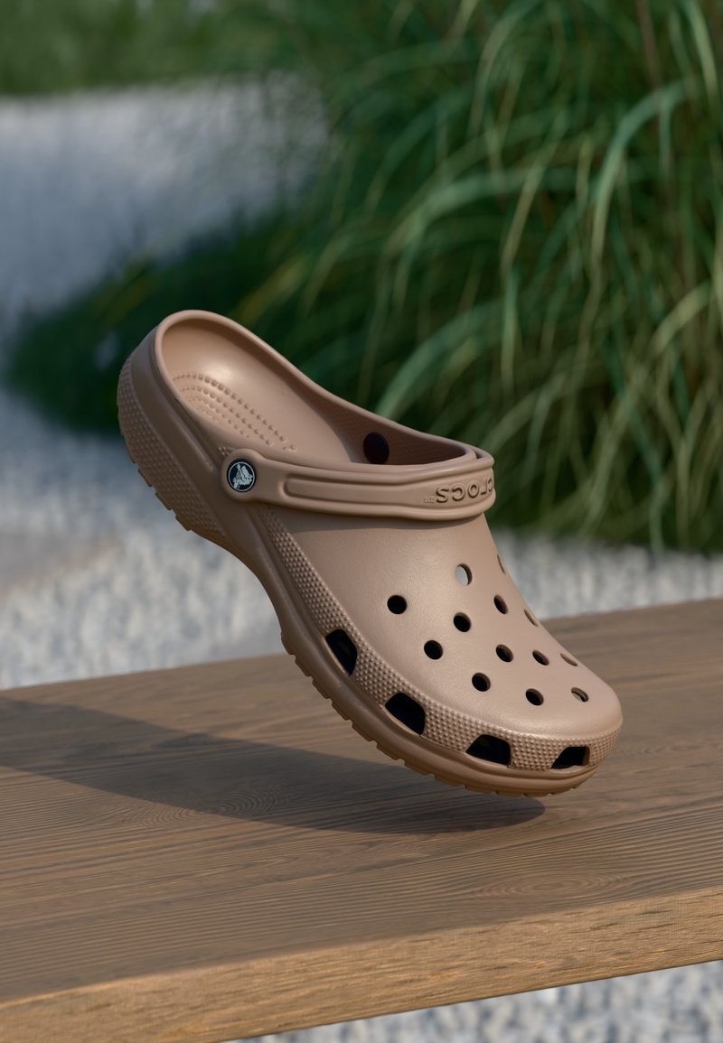 Sabots marron clair avec des trous de ventilation, semelle épaisse et sangle texturée, fabriqués en matériau plastique lisse. Présente un emblème de la marque sur le côté.