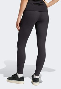 Leggings neri a costine con un design aderente, dotati di vita alta e texture liscia, abbinati a sneakers nere e calzini bianchi.