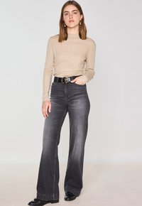 Maglione beige a maniche lunghe dalla forma aderente abbinato a jeans a vita alta svasati di un grigio scuro. Cintura nera con fibbia circolare dorata.