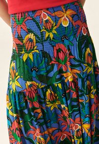 Jupe maxi florale en tissu léger, présentant des couleurs vives telles que le bleu, le vert, l'orange et le jaune, avec une taille smockée et un design en couches.