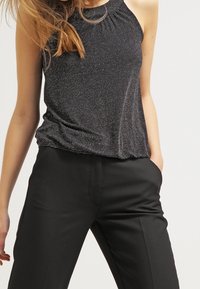 Czarny bezrękawnik z teksturowanej, połyskującej tkaniny oraz marszczonym dekoltem; sparowany z dopasowanymi czarnymi spodniami z bocznymi kieszeniami.