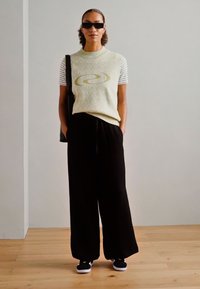 Light green and white striped short-sleeve top with a circular design, paired with black wide-leg pants and black sneakers.