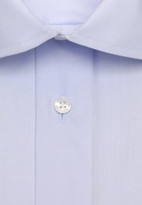 Gros plan sur le col d'une chemise bleu clair et sur le bouton supérieur fermé avec un bouton en plastique blanc à quatre trous.