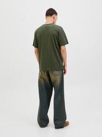 Zaļš kokvilnas T-krekls ar apaļu kakla izgriezumu, apvienots ar platām biksēm no zilajiem džinsiem, kuriem ir gradienta efekts no tumšā līdz gaišajam.