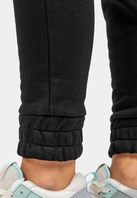 Zwarte joggers met een slim fit ontwerp, voorzien van een geribde manchet bij de enkel. Gekleed met lichtgrijze en blauwe sneakers.