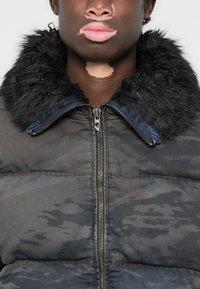 Puffer jacket in black with a textured faux fur collar, zip closure, and a subtle dark camouflage pattern across the fabric.