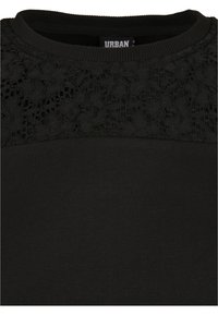 Pull noir à col rond côtelé avec un détail en dentelle florale sur le haut de la poitrine et les épaules, montrant la texture et le motif du tissu.