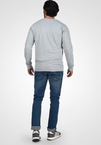 Grauer Langarm-Sweatshirt mit gerippten Bündchen, kombiniert mit dunkelblauen Slim-Fit-Jeans und grauen Sportschuhen mit weißen Akzenten.