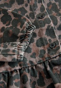 Tkanina s uzorkom smeđeg i crnog leoparda s skupljenim elastičnim manšetama i crnim gumbima na tkanom odjevnom predmetu, krupni plan.