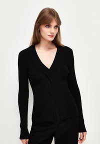 Zwarte geribbelde gebreide cardigan met een diepe V-hals, lange mouwen en een crossover-ontwerp bij de taille. Heeft een gestructureerde afwerking en een subtiele zoomdetail.
