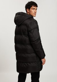 Czarna kurtka puchowa z kapturem, z poziomymi pikowanymi sekcjami, długimi rękawami i średniej długości krojem. Gładki, błyszczący materiał.