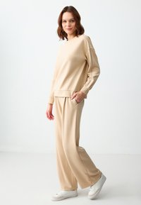 Beige sweatshirt met een ontspannen pasvorm, lange mouwen en ribbels aan de manchetten, gecombineerd met bijpassende tapered broeken, voorzien van zijzakken en een gladde textuur.