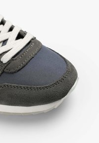 Baskets grises avec une combinaison de matériaux en daim et en tissu ; tige texturée avec des lacets et une semelle blanche contrastante.