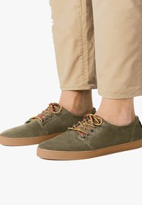 Grüne Wildleder-Sneaker mit einem niedrigen Design, ausgestattet mit kontrastierenden mehrfarbigen Schnürsenkeln und einer karamellfarbenen Gummisohle für guten Halt.