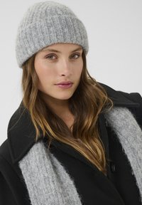 Gray knitted beanie made of fluffy material, paired with a black coat featuring a gray textured scarf. Simple design, warm and cozy appearance.