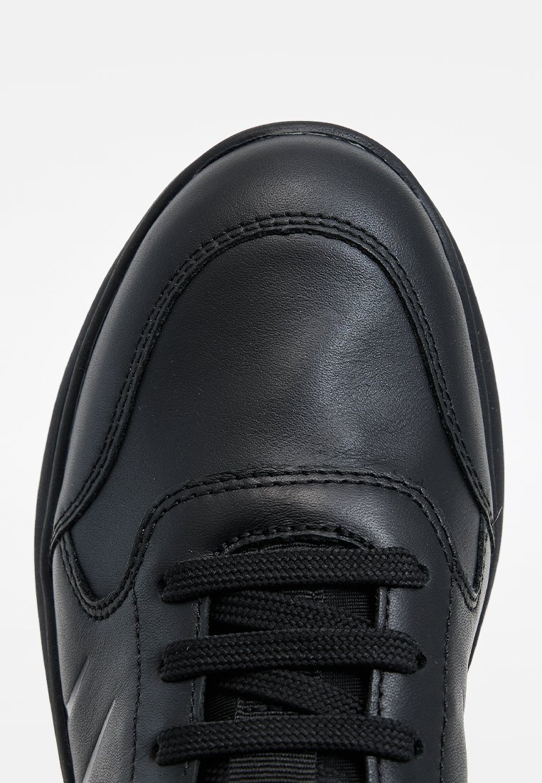Baskets en cuir noir avec une texture lisse, bout rond et lacets noirs. Présente des accents de couture et un design minimaliste.
