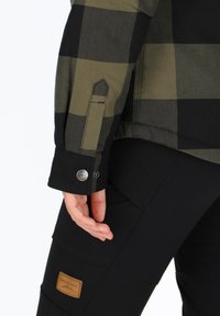 Zwarte en olijfgroene geruite overhemd met knoopmanchetten, gemaakt van een gestructureerde stof en een leren logopatch op zwarte broek.
