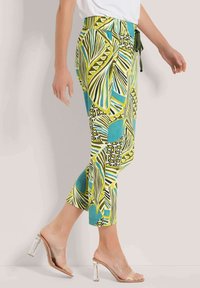 Tropenmuster-Culottes in Grün, Blau und Gelb mit elastischem Bund und Bindeband. Kombiniert mit klaren Absatzsandalen.