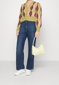 Grön, rosa och brun argyle-mönstrad stickad cardigan, samsatt med mörkblå vida jeans och en ljusgul handväska. Vita sneakers fulländar looken.