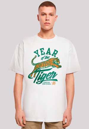 White cotton T-shirt featuring an orange and green tiger graphic, with "YEAR of the TIGER" and "HAWKINS HIGH SCHOOL '86" text.