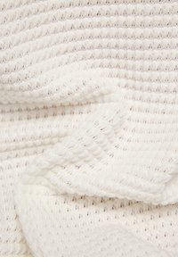 Strukturiertest weißes gewebtes Material mit einem gerippten Muster, das weiche Falten und ein leichtes Aussehen aufweist. Das Material zeigt sanfte offene Gewebe.