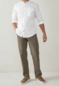 Bílá košile s mandarin límcem, náprsní kapsou a dřevěnými knoflíky, spárovaná s olivovými kalhotami a hnědými semišovými botami.