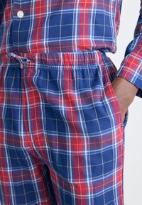 Conjunto de pijama a cuadros con patrón de cuadros en rojo, azul y amarillo. Tela suave, cintura elástica y bolsillos laterales. Detalle de camisa abotonada.