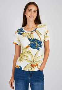 T-shirt blanc à manches courtes avec un imprimé tropical coloré comprenant des oiseaux bleus et des feuilles de palmier jaunes. Fabriqué en tissu en coton doux.