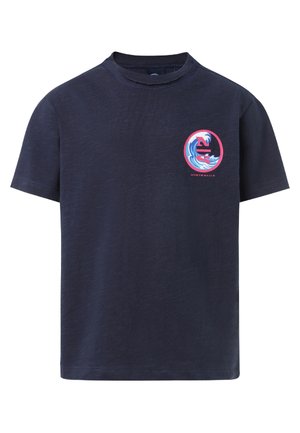 Kind trägt ein marineblaues T-Shirt mit Wellenmotiv und passende Cargo-Shorts, steht mit einer Hand in der Tasche und weißen Sneakern.