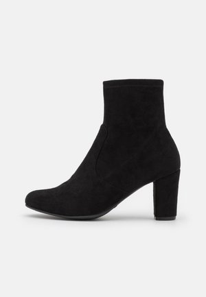 Botte de cheville en suède noir avec un bout arrondi et un talon bloc effilé. Présente une texture lisse et un détail de couture sur le côté pour la structure.