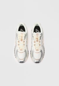 Scarpe da ginnastica bianche e argento con tomaia in rete, lacci crema e dettagli rosa. Presentano un collare imbottito e una soletta nera con logo.
