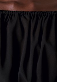 Tissu noir à la texture douce, avec une taille froncée pour un ajustement élastique. Le matériau semble léger et fluide.