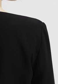 Černý oděv se strukturovanými rameny, hladkou texturou a minimalistickým designem. Disponuje zaobleným výstřihem a čistým zpracováním.