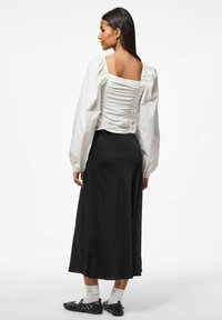 Hvid bluse med puffærmer og ruched detalje på ryggen, kombineret med en lang sort nederdel og sorte flade sko, der har ankelhøje hvide sokker.