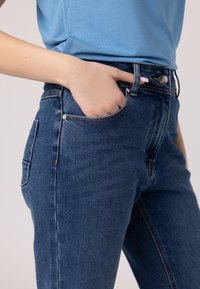 Jeans in denim blu con vestibilità slim, dotati di tasche anteriori e posteriori, chiusura con zip e cuciture decorative lungo le cuciture.