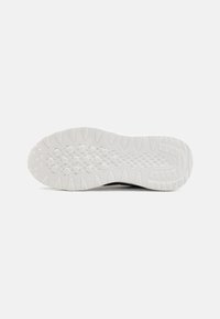 Black athletic shoe sole with a textured white rubber bottom, featuring a patterned tread for grip and traction, designed for performance.