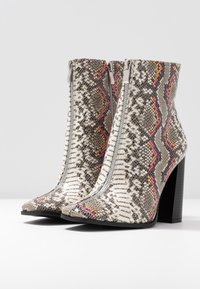 Hoge enkelboots met een nep-snakeprint in wit, grijs en roze, voorzien van een voorrits en een chunky zwarte hak.