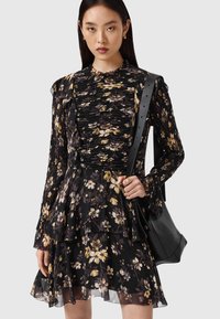 Vestido negro con estampado floral que presenta un corpiño con volantes, mangas largas, falda de capas y textura translúcida. Combinado con un bolso negro.
