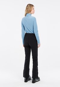Maglietta blu a maniche lunghe con colletto alto, abbinata a pantaloni da sci neri. I pantaloni hanno un design elegante e cerniere laterali, completati da stivali da sci neri.