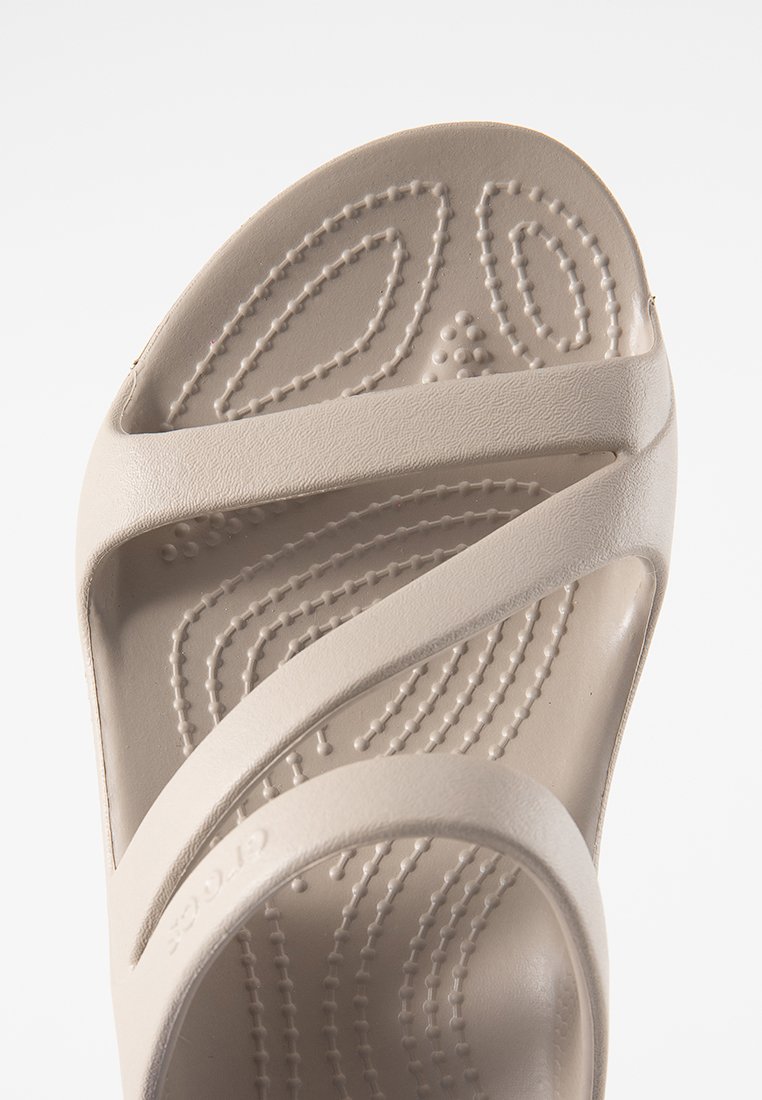 Beżowe klapki z krzyżowym paskiem i fakturowaną wkładką. Wykonane z gładkiego materiału, z delikatnym logo.