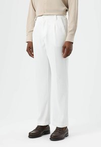 Witte broek met krijtstreep, hoge taille en voorplooien, gecombineerd met donkerbruine loafers en een beige overhemd met knopen.